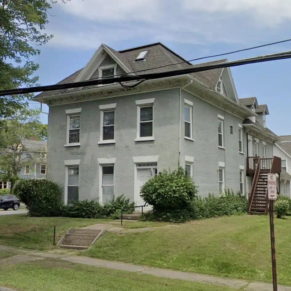 a large gray house with white trim and a brown roof. The house has several windows and a small staircase leading to the front door.