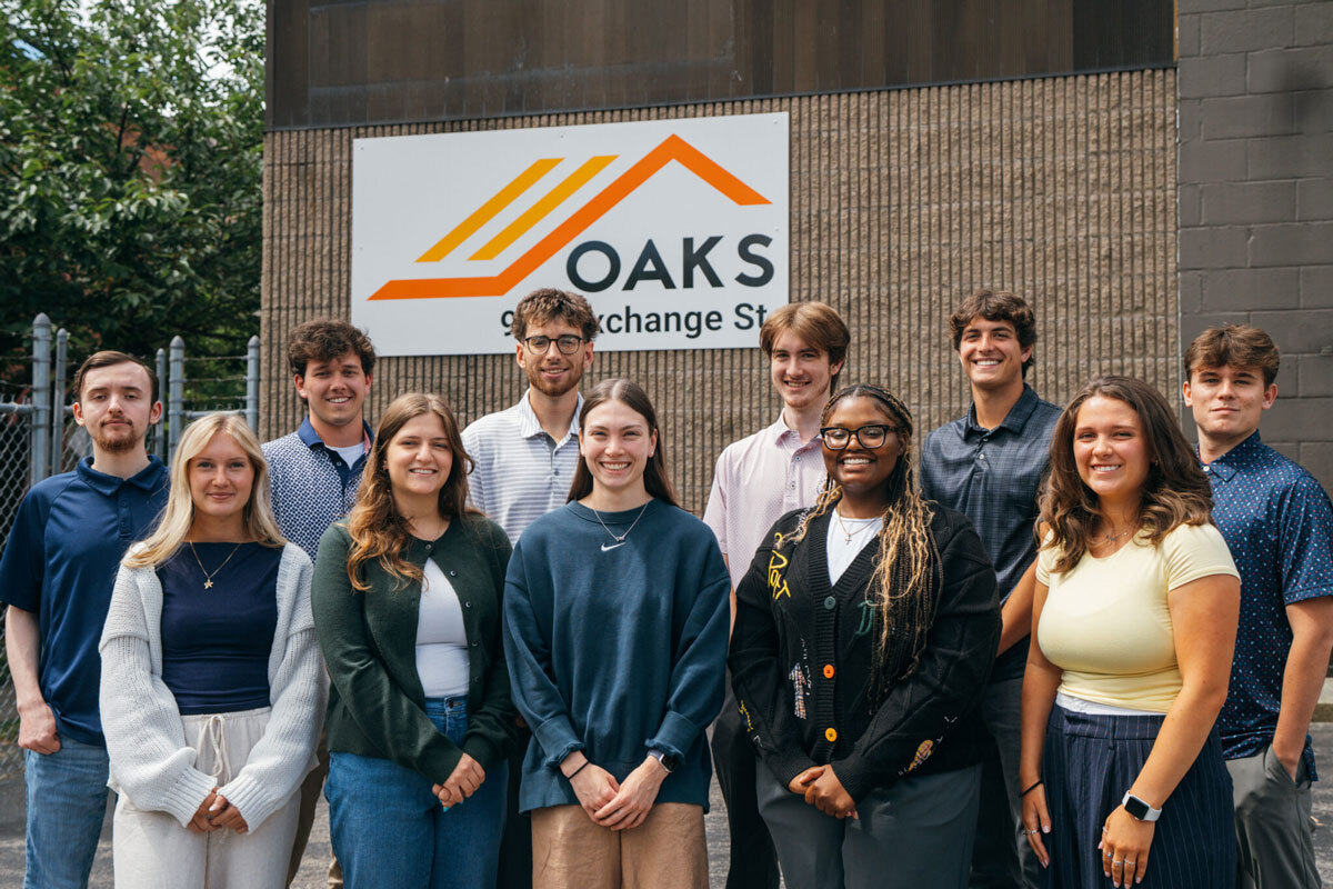 Group of young adults standing in front of building, OAKS Exchange sign
