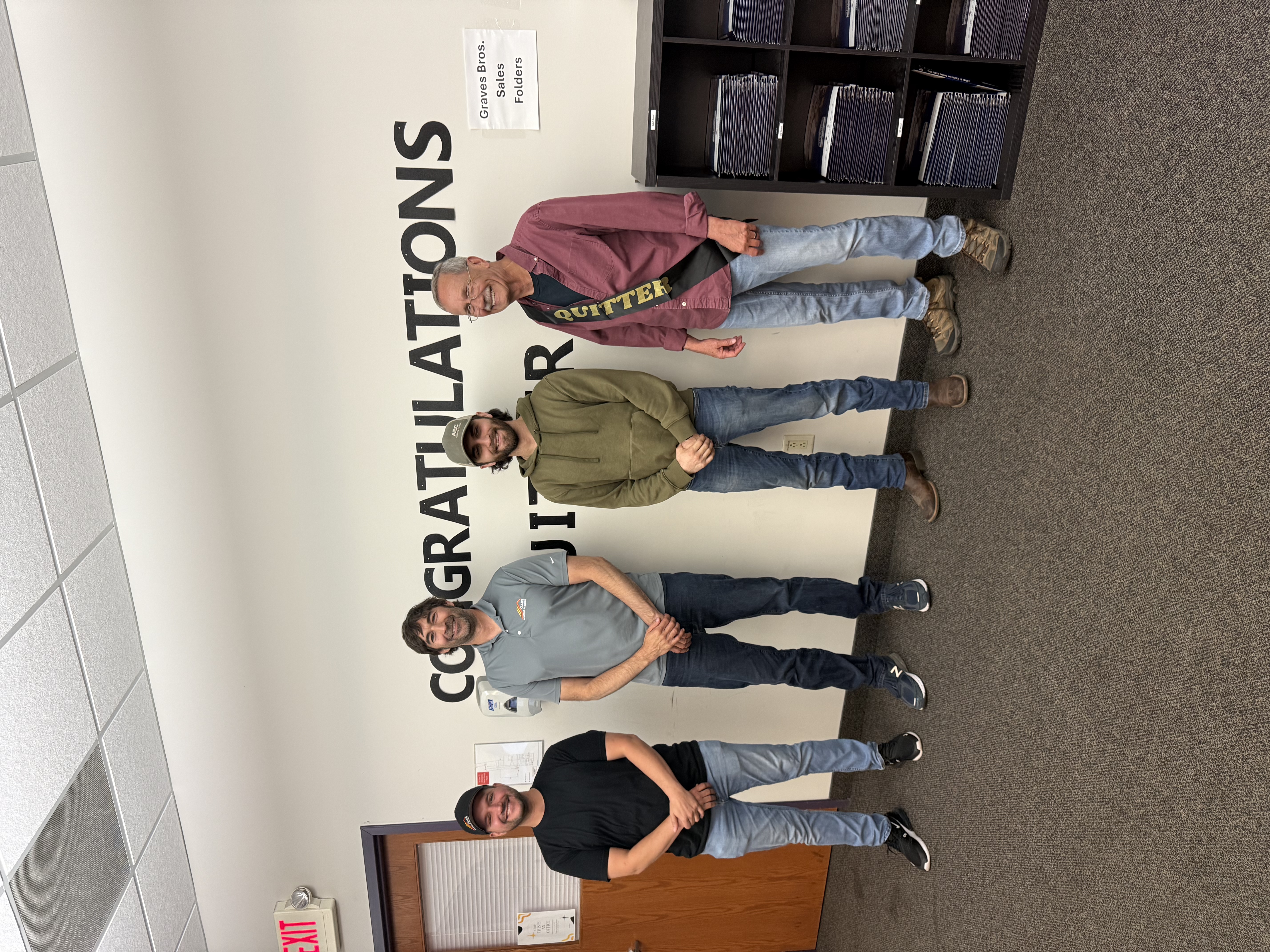 Four men standing together smiling. They appear to be in an office setting.