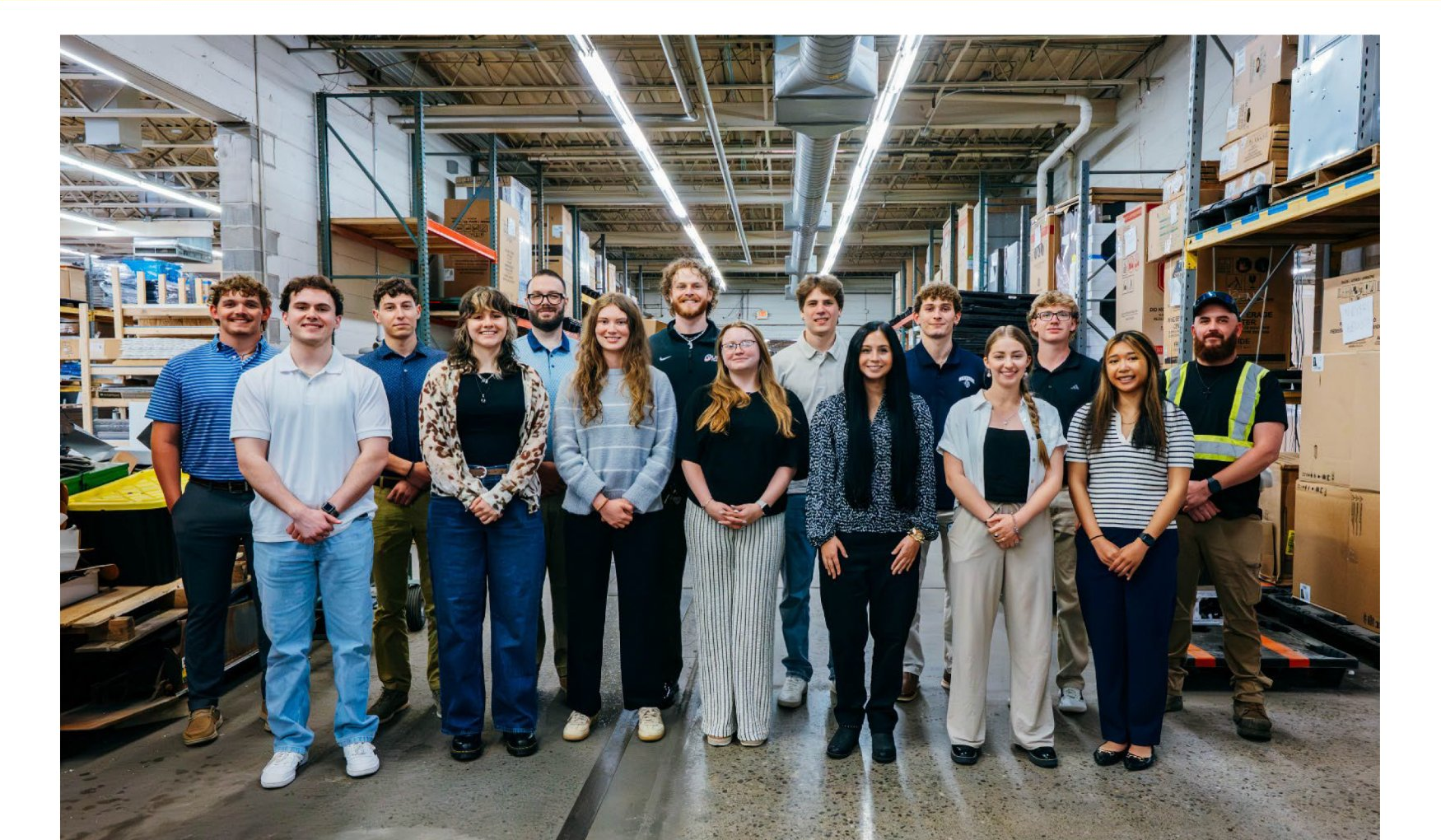 A group of people standing in a warehouse. They are smiling and looking at the camera.