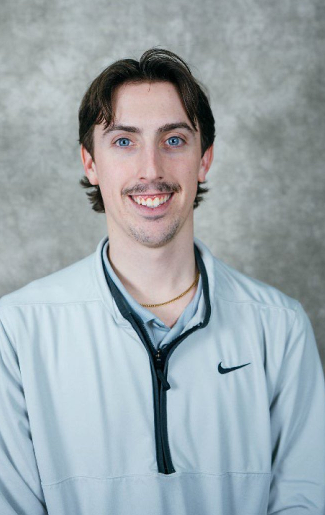 A young man with brown hair and a warm smile wearing a light blue Nike sweatshirt.
