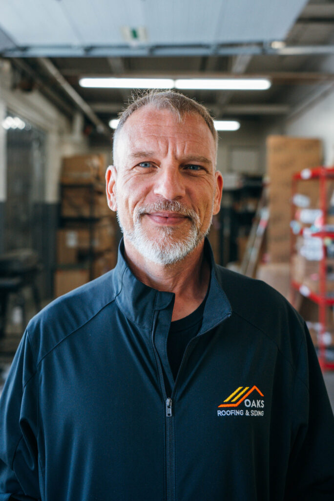 A man with a short hair and a slight smile wearing a navy blue jacket with a MARS Logistics Group logo. He appears to be in a warehouse setting.