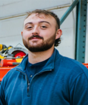 A man with a beard wearing a blue shirt. He appears to be in a workshop.