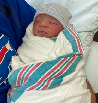 A newborn baby swaddled in a white blanket with blue and red stripes. The baby is sleeping peacefully.