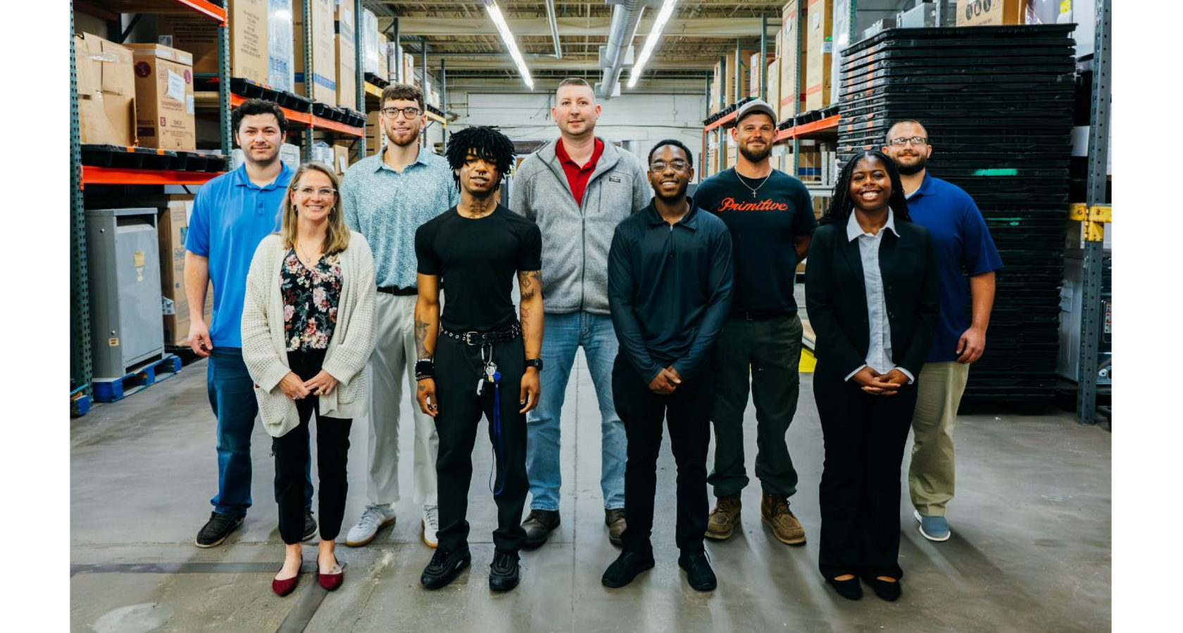 A diverse group of people standing together in a warehouse. They appear to be employees or team members.