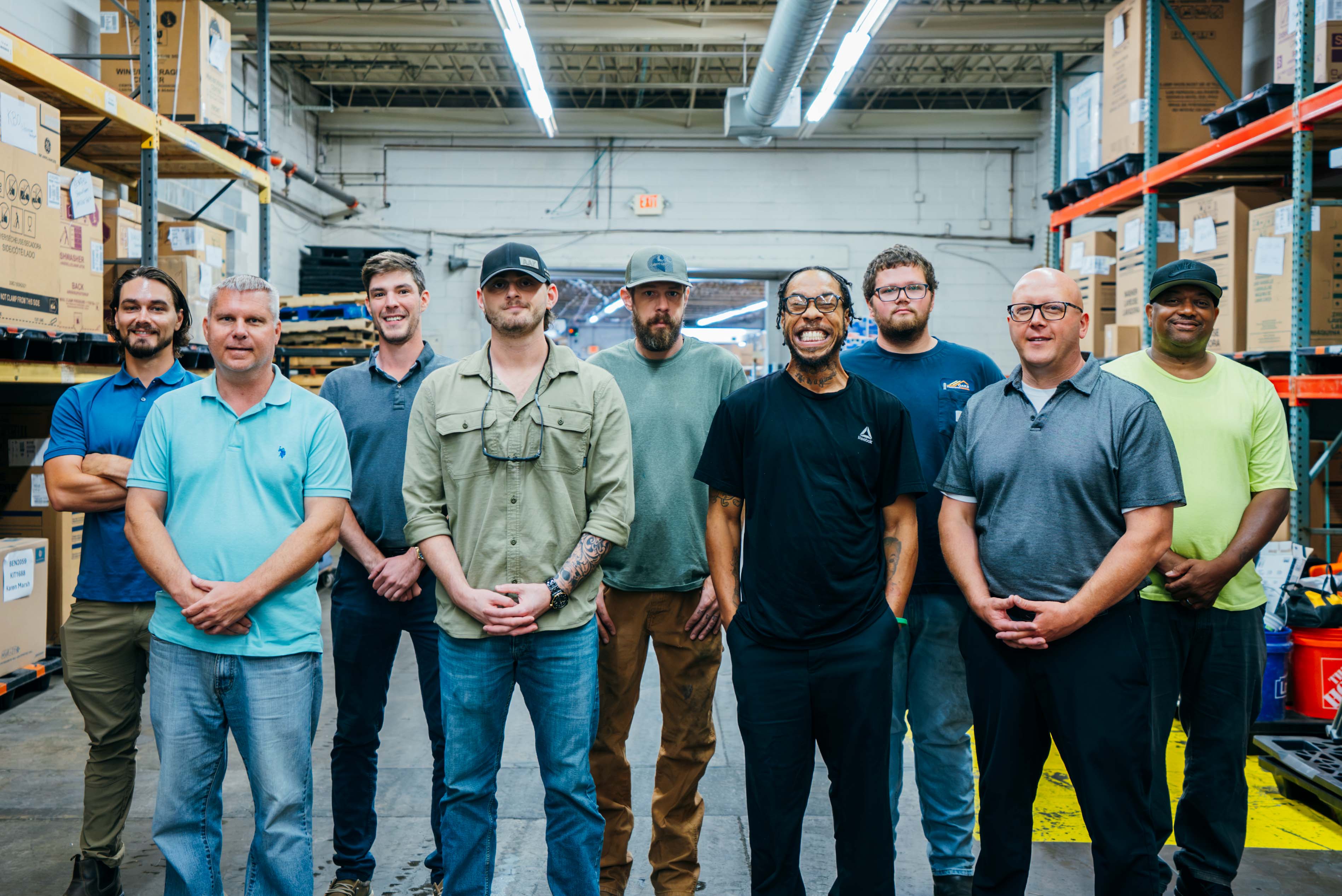 A group of dedicated warehouse staff standing together amidst organized shelves and boxes. The team appears ready for work in a well-lit and spacious environment.