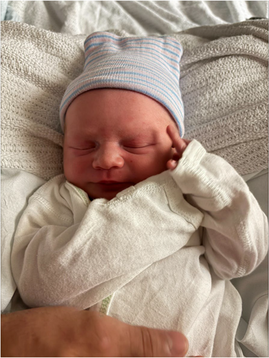 A serene newborn baby sleeps peacefully, dressed in a striped hat and snug white outfit, cradled in a cozy white blanket.