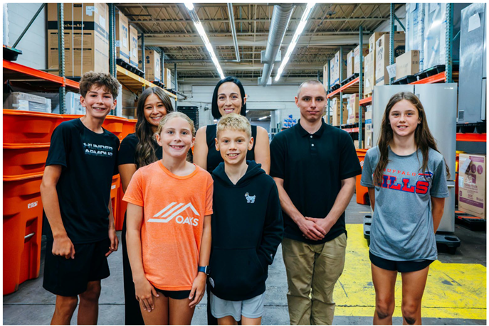A group of kids standing in a storage unit facility with orange bins and shelves in the background.