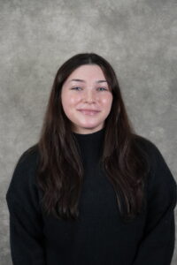 A smiling woman with long dark hair wearing a black sweater against a neutral gray background.