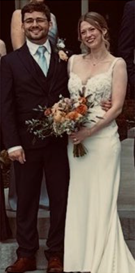 Marilyn Freetheart in a white wedding dress with her groom, holding a bouquet of orange and white flowers.