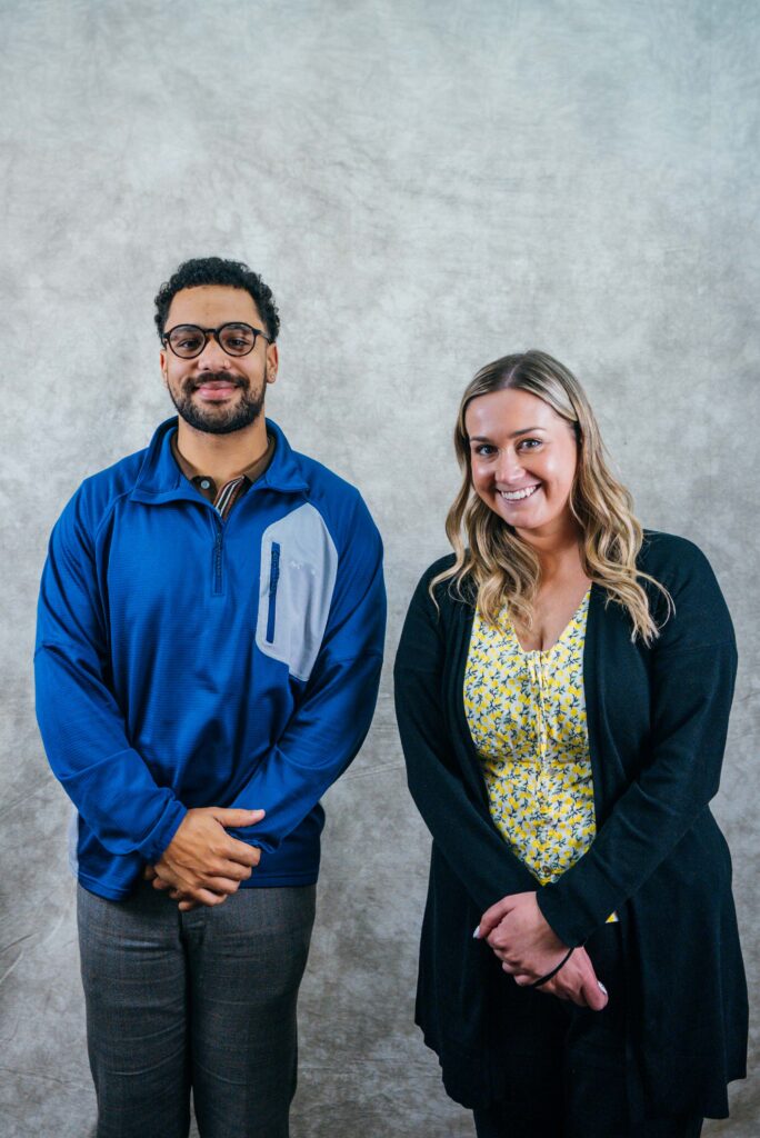 Professional headshot of a man and a woman standing side by side. Both are dressed in business casual attire and smiling at the camera.