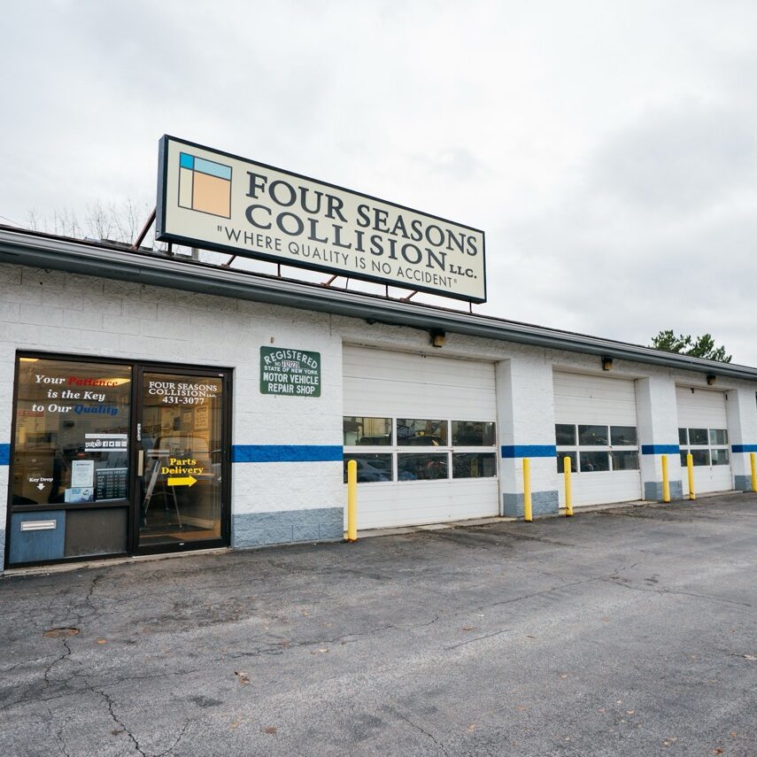 A white auto body shop with blue stripes and a sign reading Four Seasons Collision