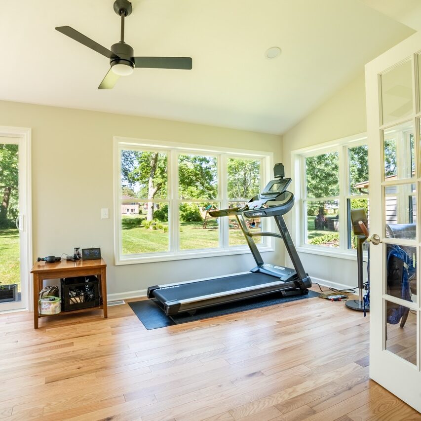 A home gym with a treadmill and exercise equipment. Large sliding glass doors lead to a backyard.