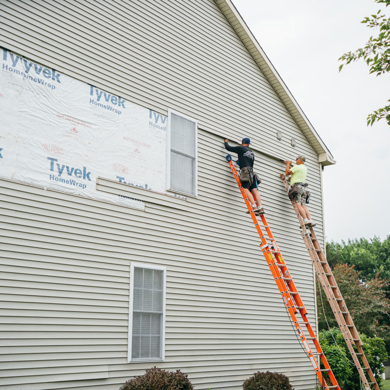 Workers on ladders installing siding on a house exterior.