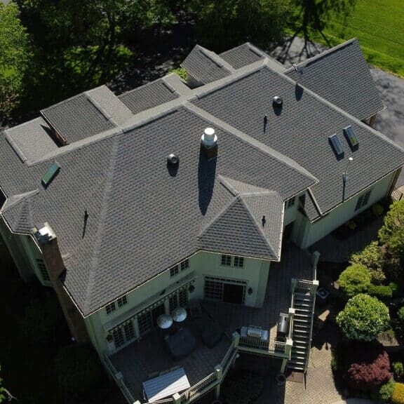 A large house with a gray roof and green lawn. The house has a chimney and several skylights.