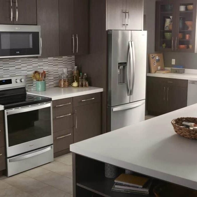 A modern kitchen with a large island, stainless steel appliances, and dark brown cabinets. The kitchen is well lit with natural light.