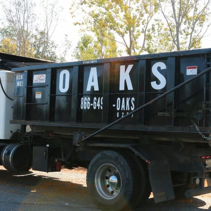 A black dump truck with Oaks logo and phone number. The truck is parked on a road.