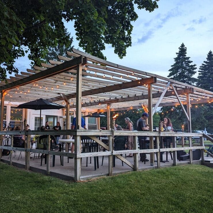 A spacious outdoor dining area with a pergola and string lights. People are seated at tables under the pergola.