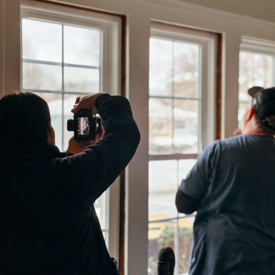 Two people taking photos through a window. They are capturing a scene outside.