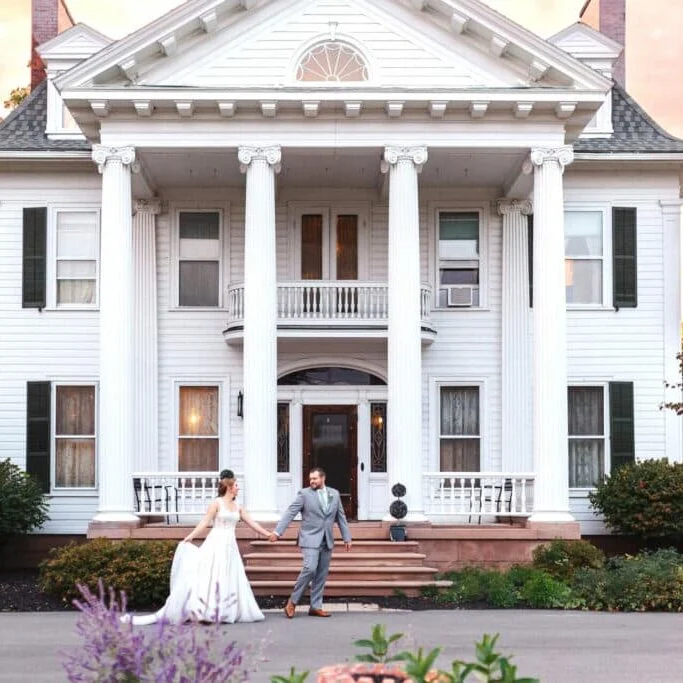 Happy wedding couple standing in front of large white house. Bride and groom enjoying romantic moment.