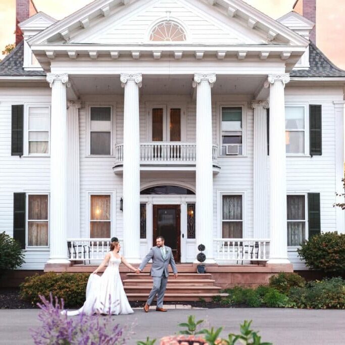Bride and groom posing on the steps of a large house. A beautiful wedding scene.