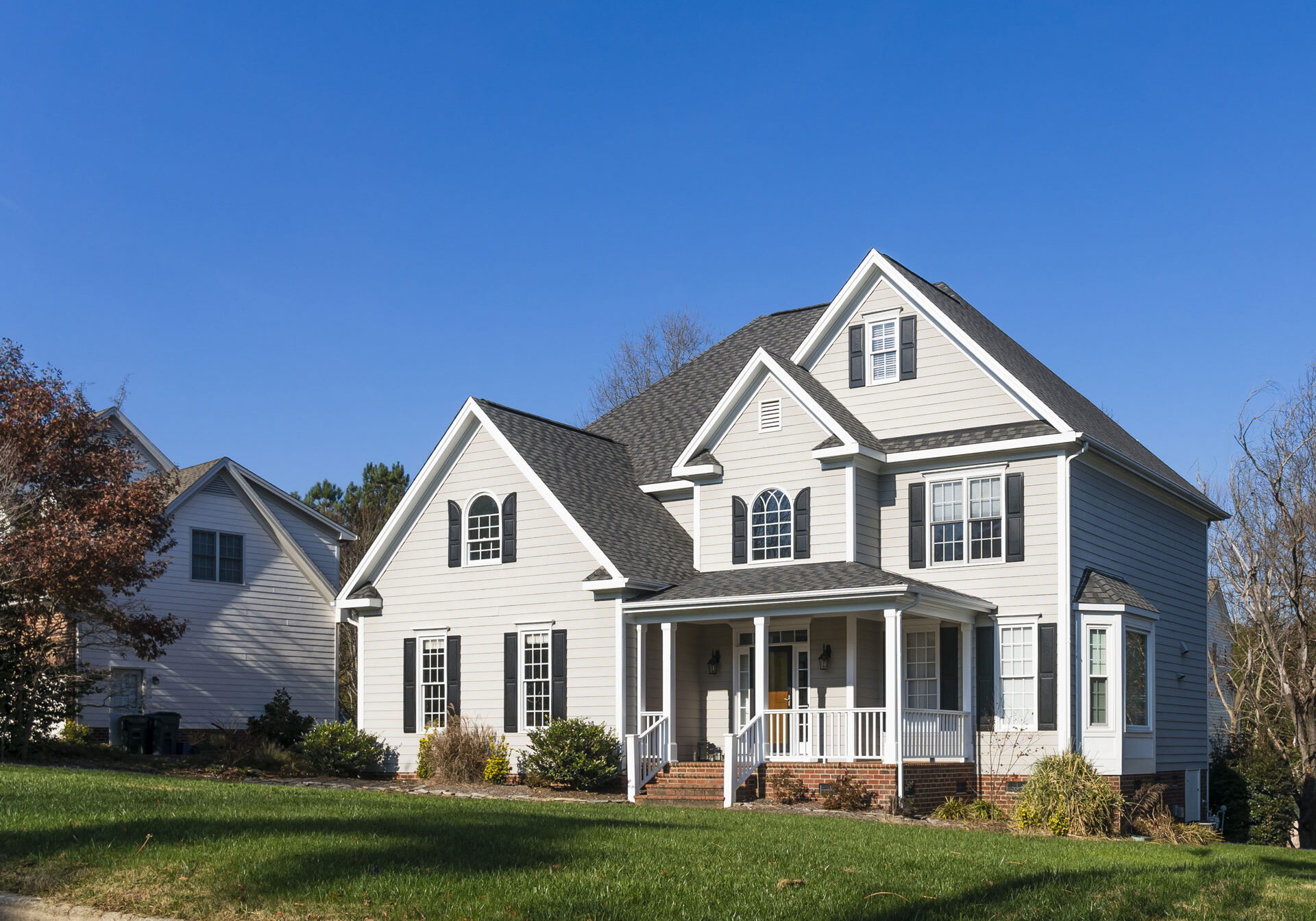 Large white house with a covered porch and green lawn. The house has two stories with multiple windows.